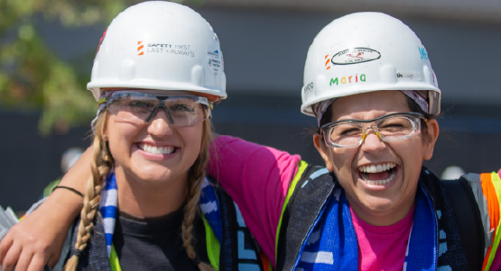 Two women smiling in hard hats on the construction site