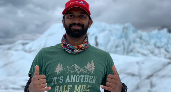 Electrical manager Jeswin Geevarughese standing in front of a glacier after hiking with a "It's a half mile or so further."