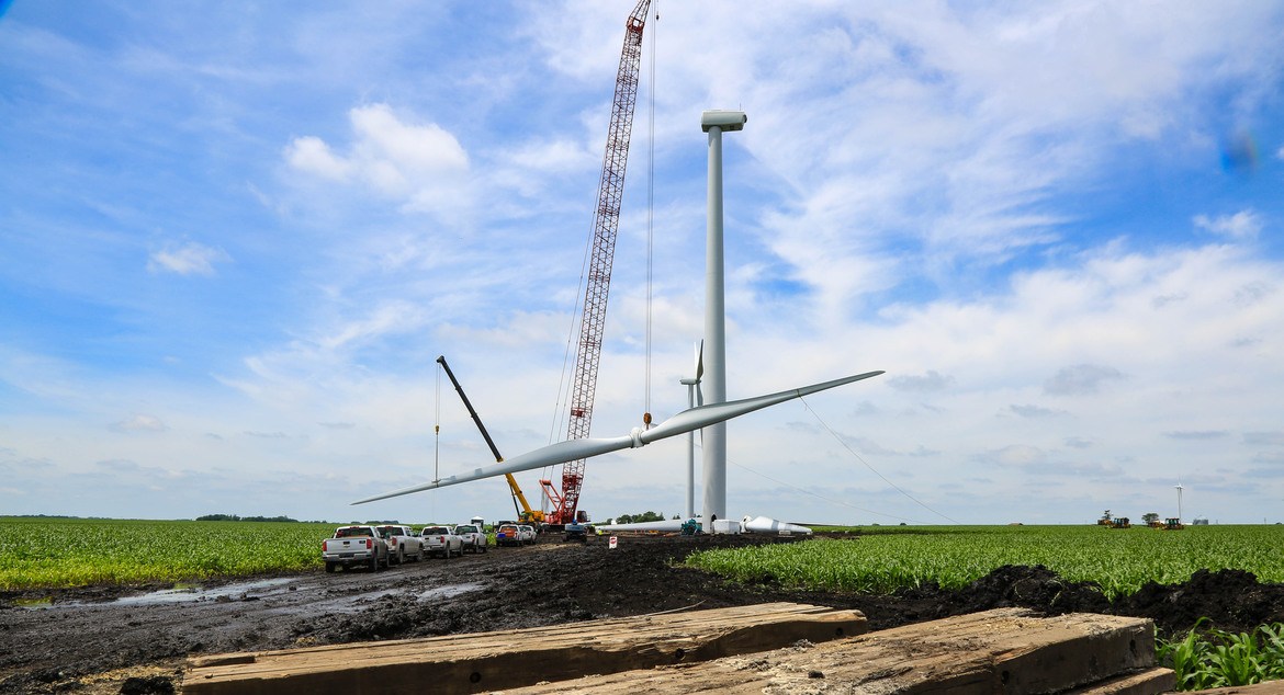 crane lifting turbine blade against blue sky