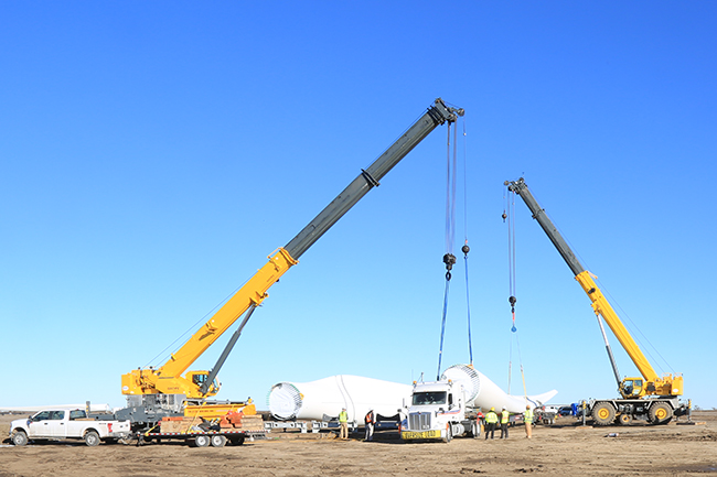 two cranes lifting turbine blade against bright blue sky