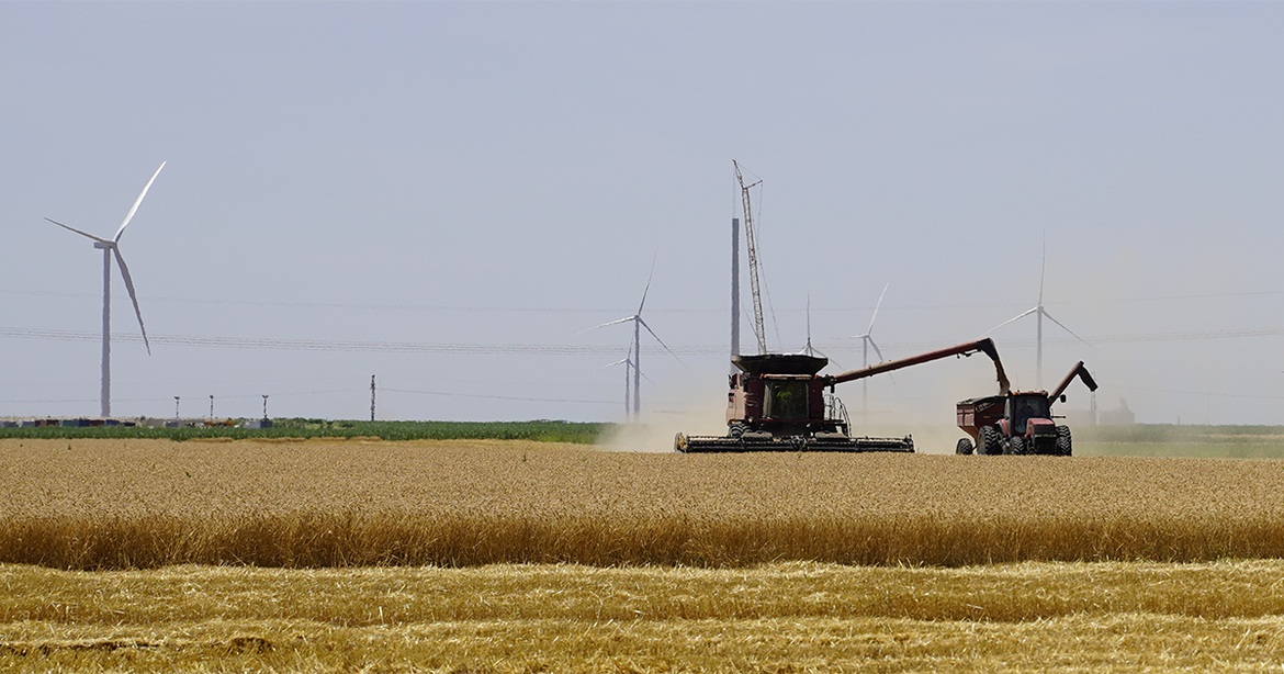 farming combine on field with wind turbines in background