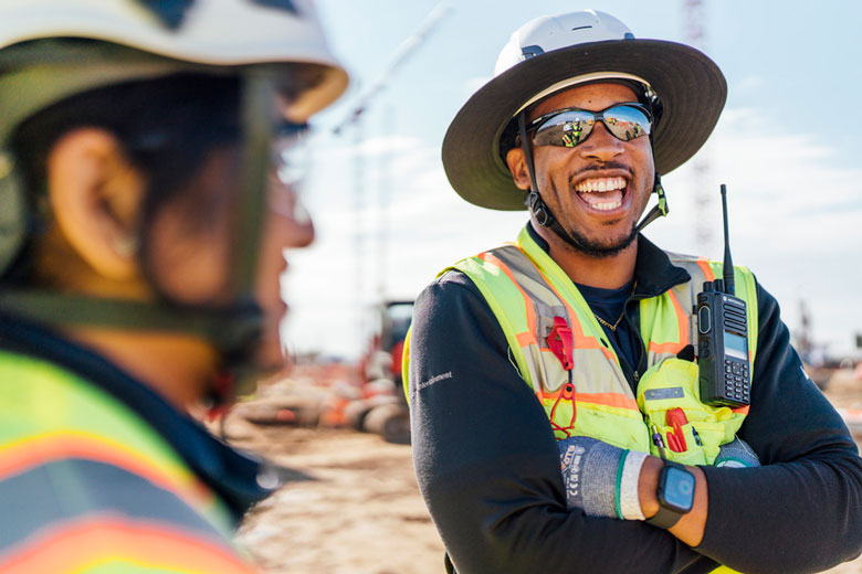 Man in construction safety helmet and sunglasses laughing with co worker