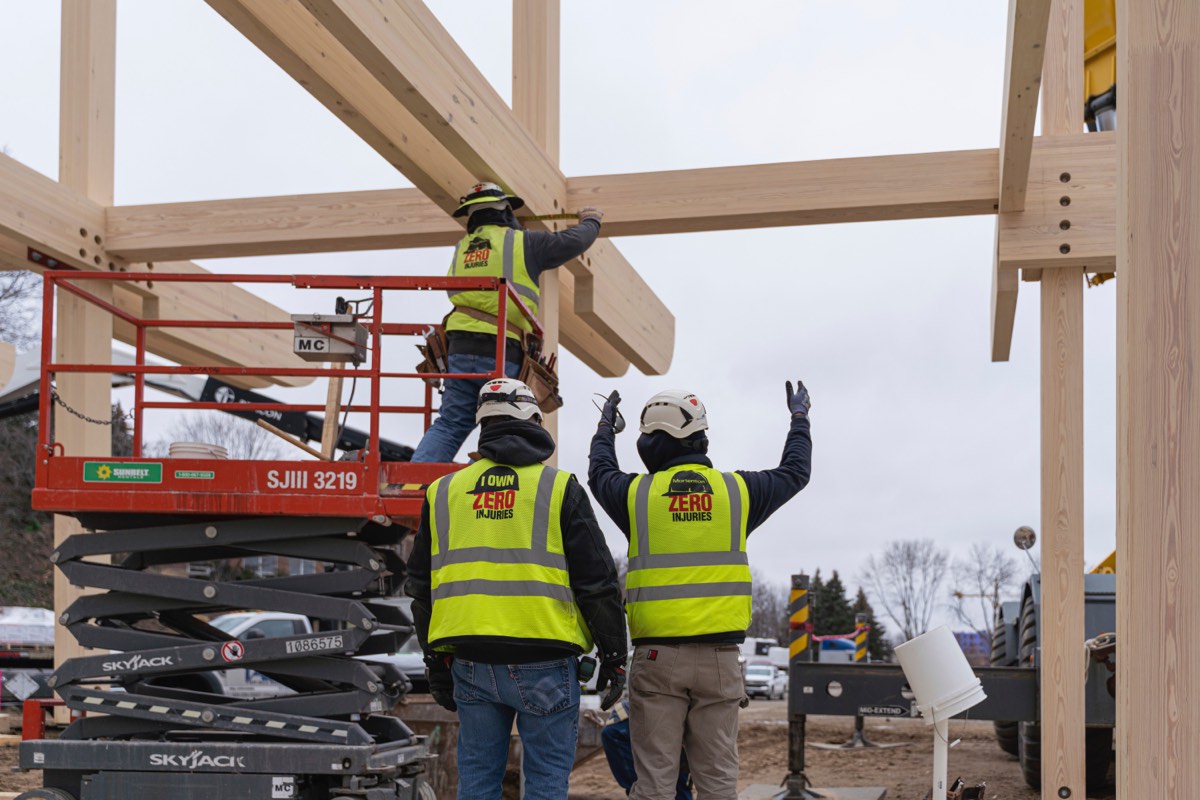 three people in construction safety vests and helmets setting beams using a lift