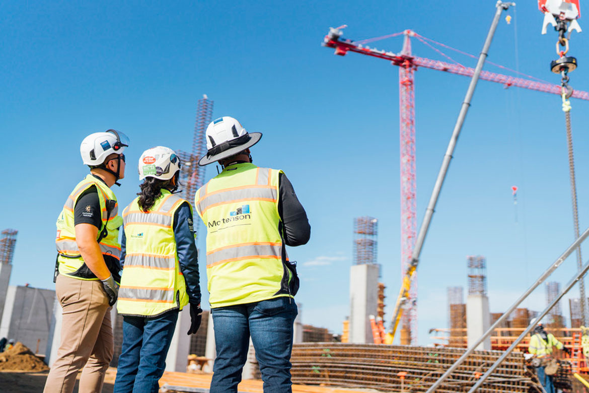 Three people in construction safety gear looking at a crane on a jobsite