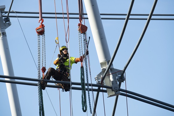 Ironworker suspended above Allegiant Stadium erecting the cable net roofing system.